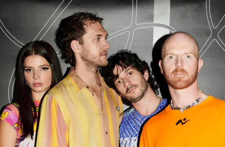Australian indie rock band The Jungle Giants posing close together in colorful outfits against a black backdrop for a band promotional photo shoot.